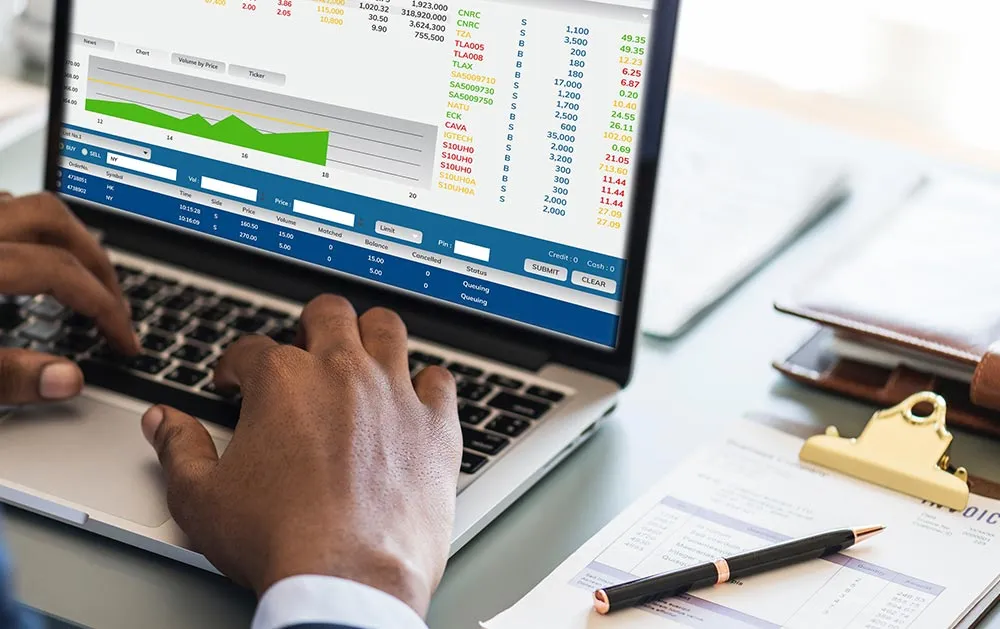 Investment information displayed on a laptop beside financial documents